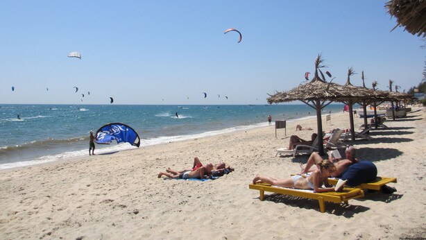 Una playa con gente tomando el sol y practicando parasailing.