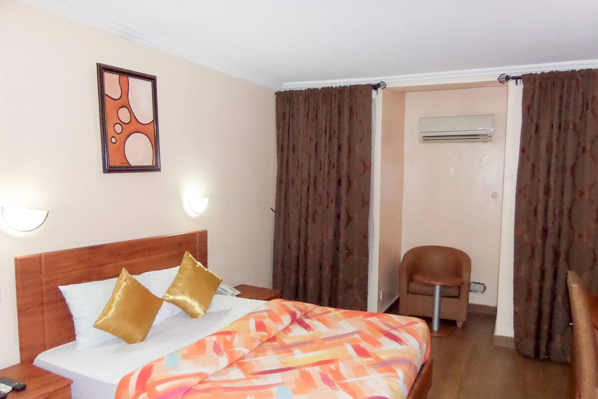 A hotel room with a bed, a chair, and an air conditioning unit.