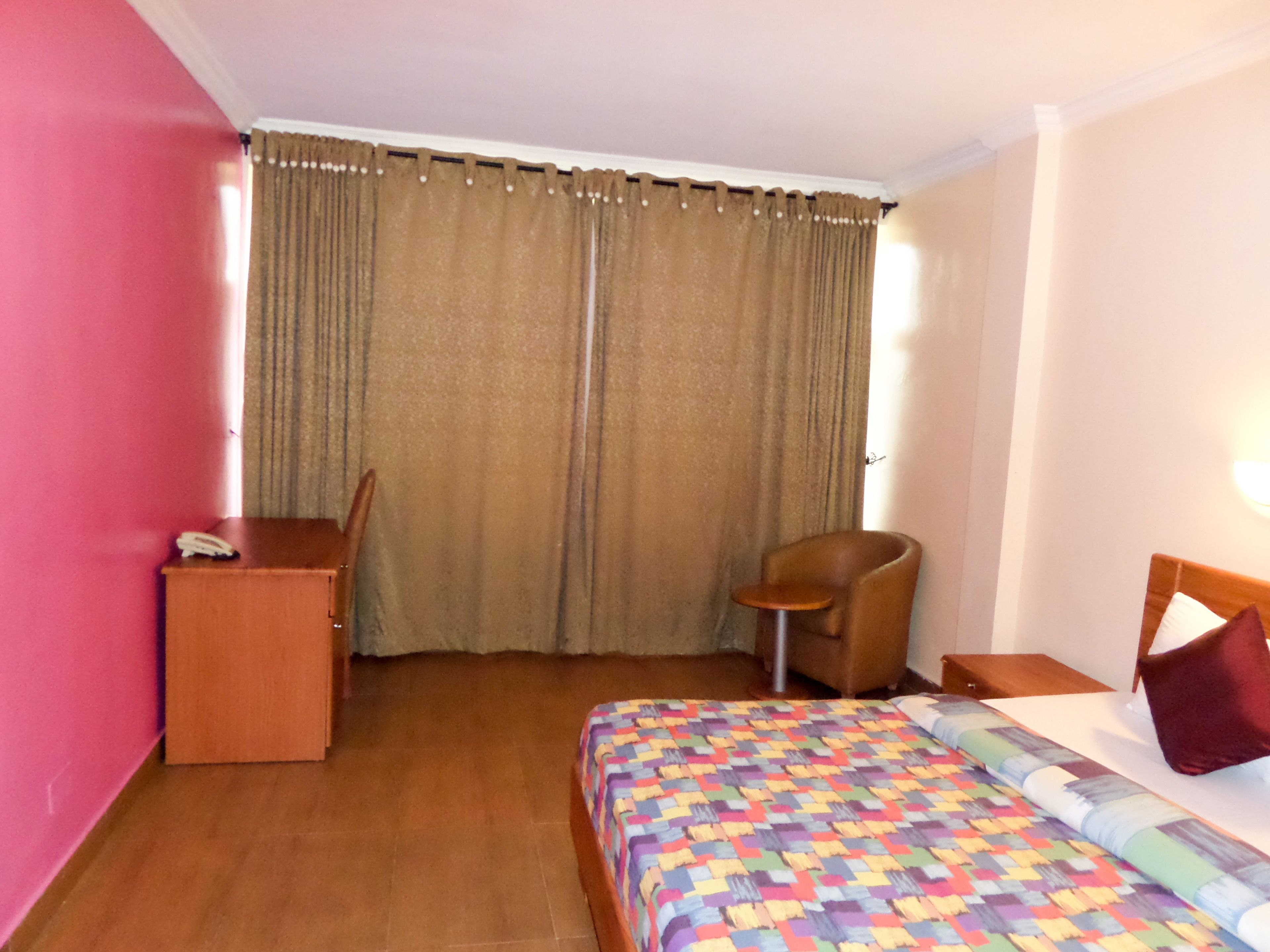 Habitación de hotel con cama, escritorio, silla y ventana con cortinas.
