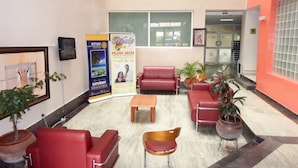 A lobby with red leather sofas, a wooden coffee table, and potted plants. There are two posters on the wall advertising events. - Le Real Hotel (Lekki)