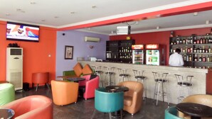 A bar area with colorful seating, a television, and a bar stocked with bottles. - Le Real Hotel (Lekki)