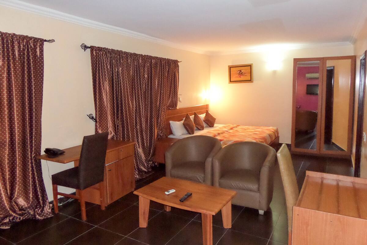 A hotel room with a bed, two armchairs, a desk, a small table, and a mirror.
