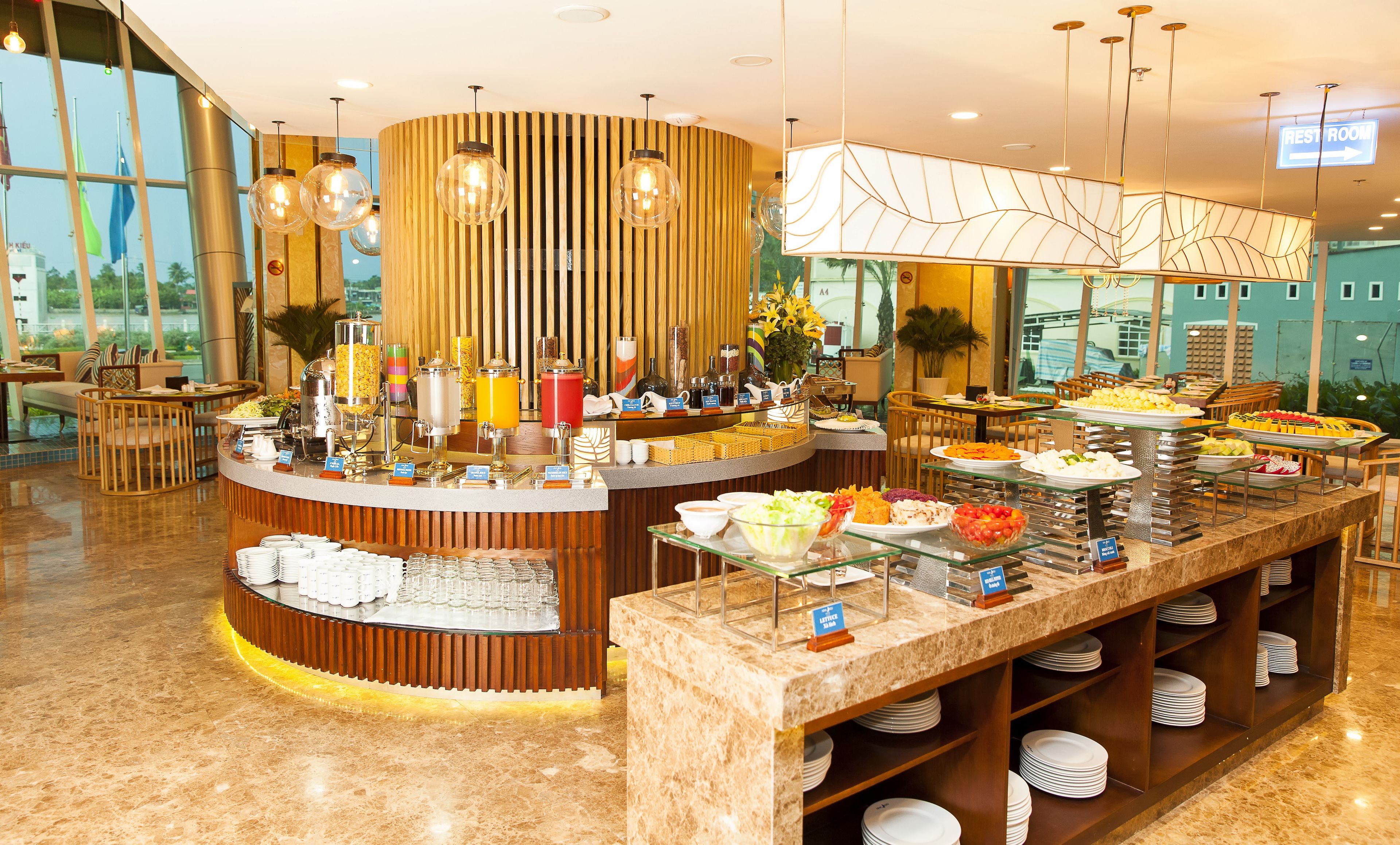 A buffet area with various food stations, a seating area with tables and chairs, and a view of the outdoors through large windows.