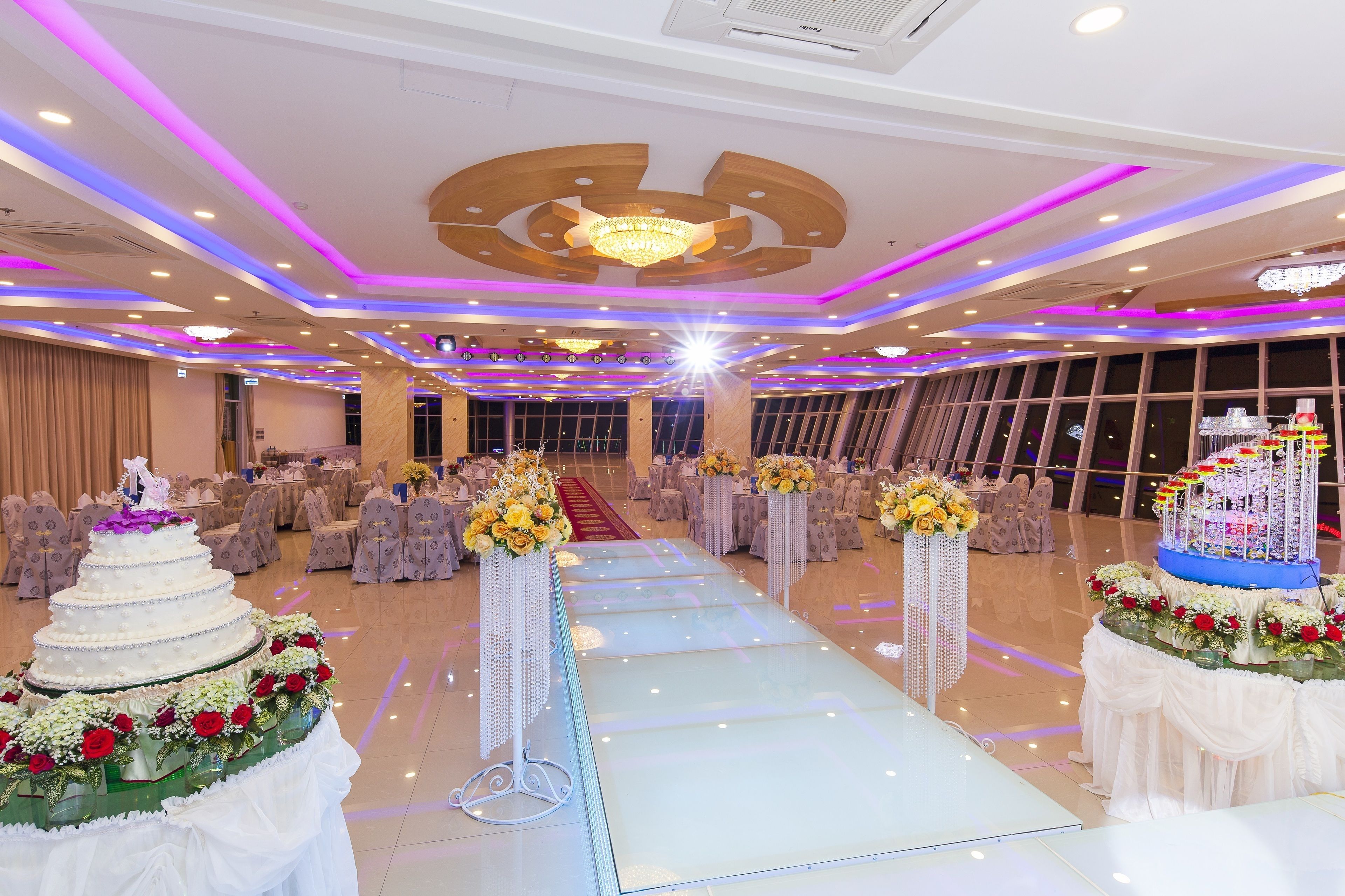 Um salão espaçoso com uma passagem central, decorado com arranjos florais e uma mesa de doces em vários níveis.