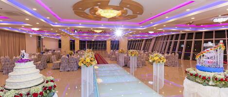 Um salão espaçoso com uma passagem central, decorado com arranjos florais e uma mesa de doces em vários níveis.