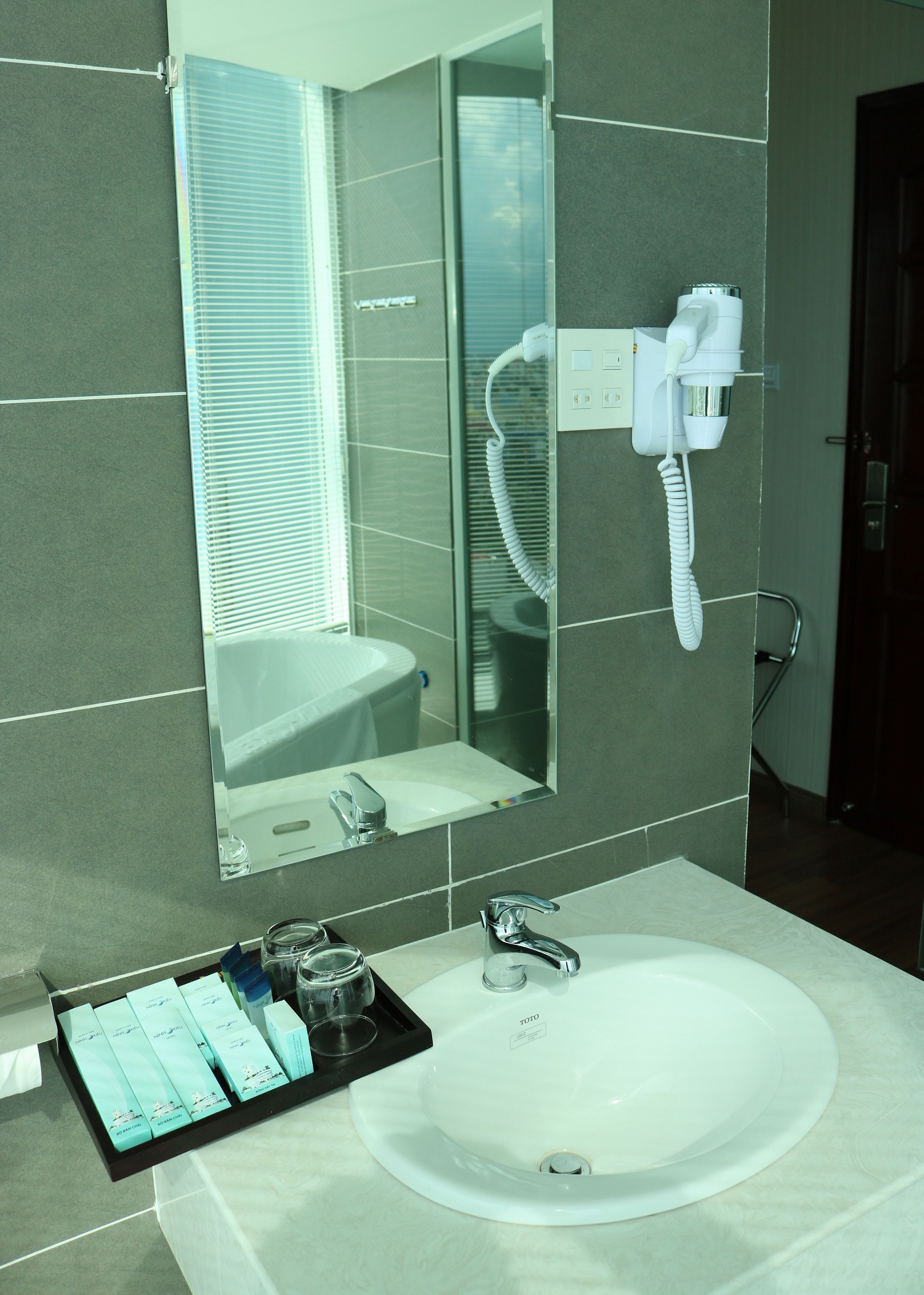 A bathroom with a white sink, a mirror, and a hairdryer mounted on the wall.