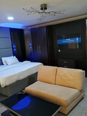 A modern bedroom with a bed, a sofa, a TV, and a unique ceiling light fixture. - Paris Suites (Lagos)
