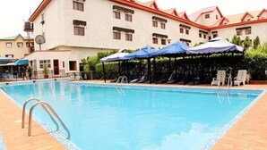 A swimming pool with sun loungers and umbrellas, surrounded by a building with multiple windows and a red roof. - Rockview Hotel Festac (Lagos)