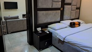 A hotel room with a large bed, a bedside table with a phone and a book, a flat-screen TV mounted on the wall, and a separate seating area with a couch and a pillow. - Rockview Hotel Festac (Lagos)