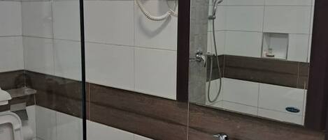 Un baño con mampara de vidrio, lavabo blanco, inodoro y espejo con luz superior.