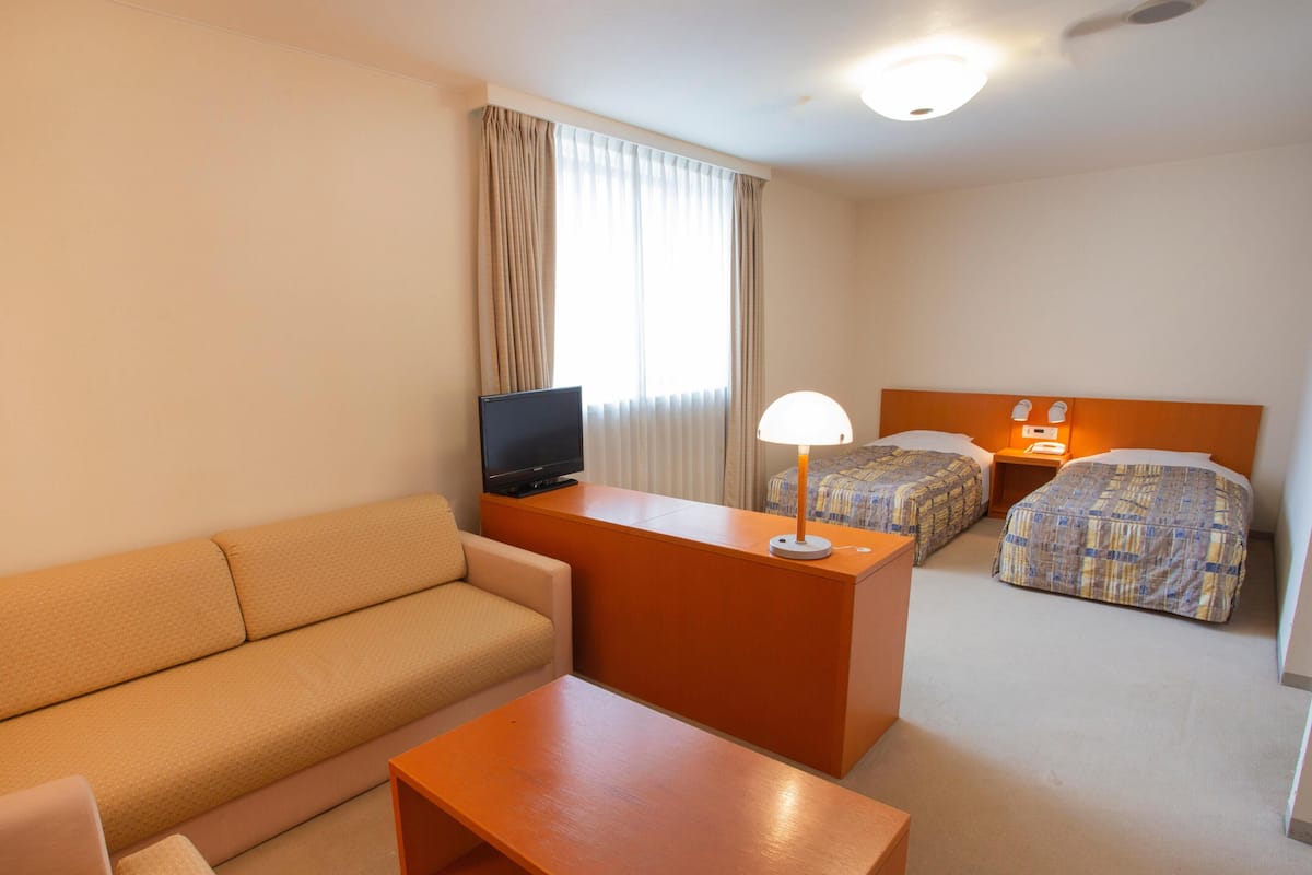 Une chambre d’hôtel avec un canapé, une petite table, une télévision, deux lits et une table de chevet avec une lampe.