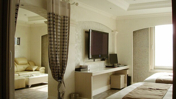 Une chambre d’hôtel comprenant un lit, un bureau avec un ordinateur, une télévision et un coin salon avec un fauteuil et un canapé.