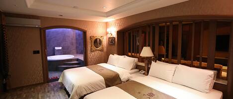 A hotel room with two beds, a bathroom with a shower, and a small sitting area with a lamp.