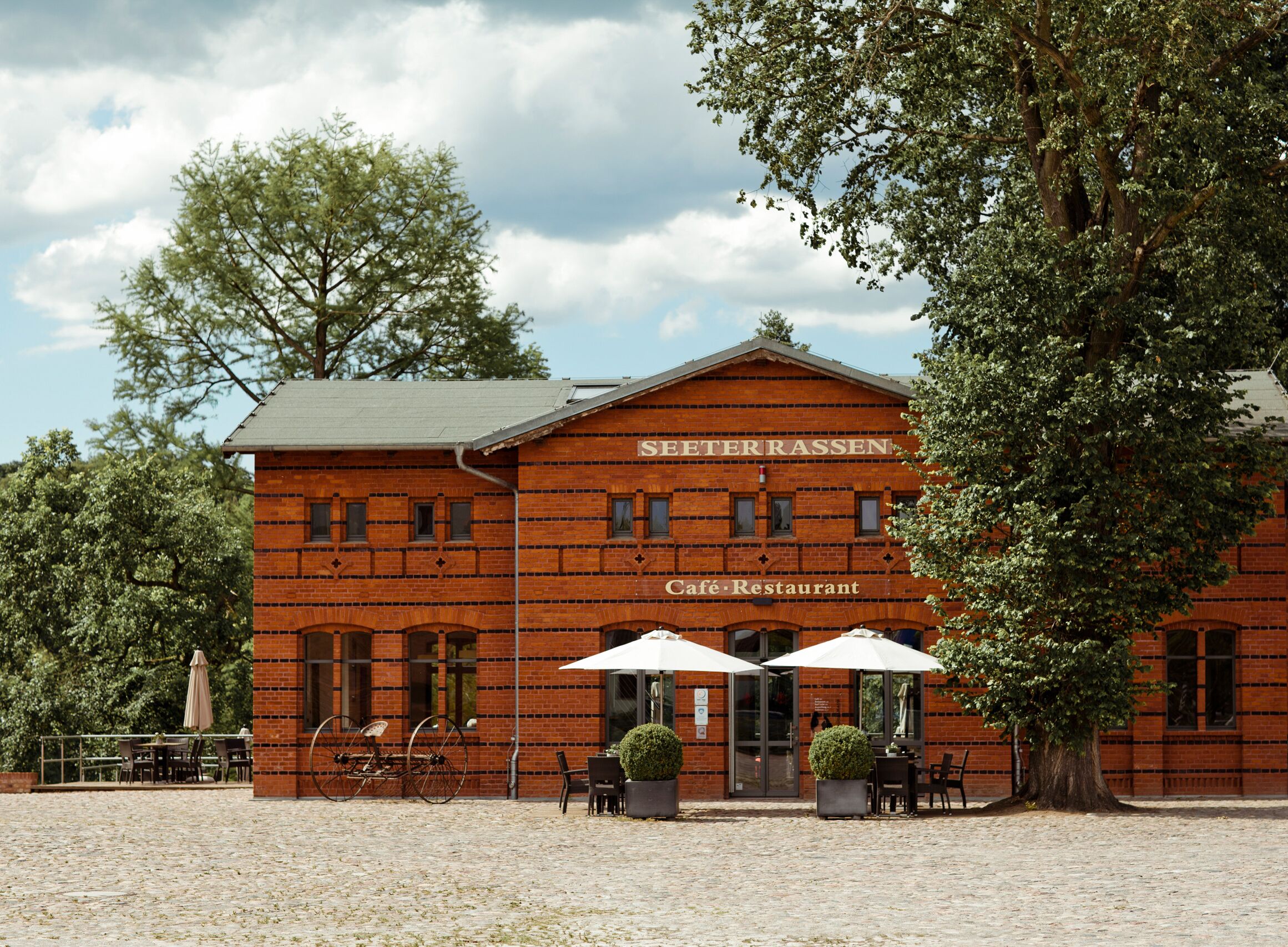 Een gebouw van baksteen met het bord 'SEETERRASSEN Café-Restaurant' en terras met parasols.