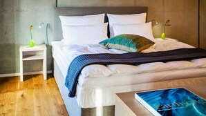 A neatly made bed with white linens, a blue and green patterned pillow, and a book titled "Earth's Pie" on a bedside table.
