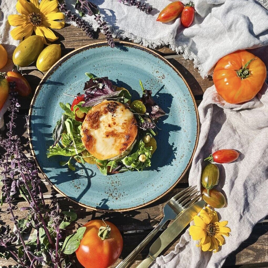 Un plato de comida sobre una mesa de madera con un plato azul, rodeado de diversas verduras y flores.