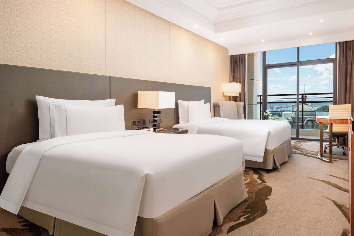 A hotel room with two beds, a desk, and a view of the city.