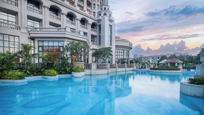 Un hotel gran i de moltes plantes amb una piscina central, envoltat de vegetació exuberant i una vista panoràmica del capvespre.