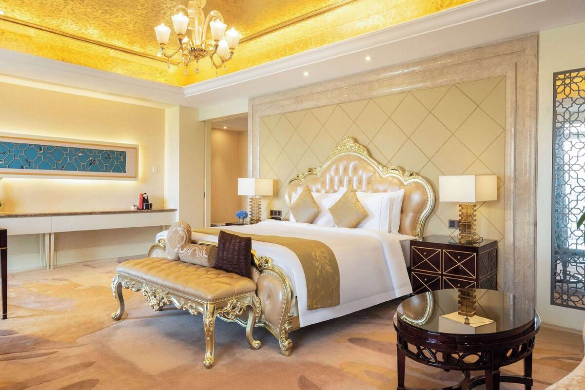 A luxurious bedroom with a large bed, ornate headboard, and a round table with a lamp.