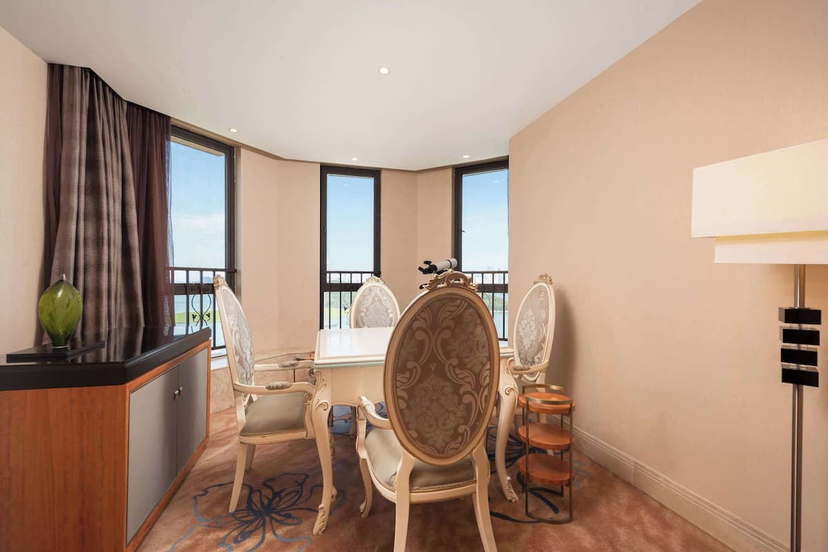 A hotel room with a dining area, a large window, a balcony, and a lamp.