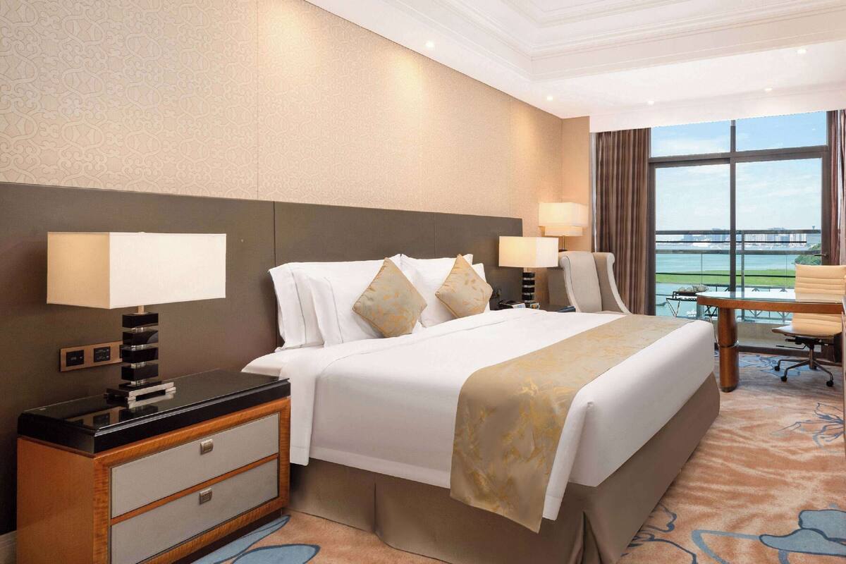 A hotel room with a large bed, two bedside lamps, a desk with a lamp, and a view of the water.