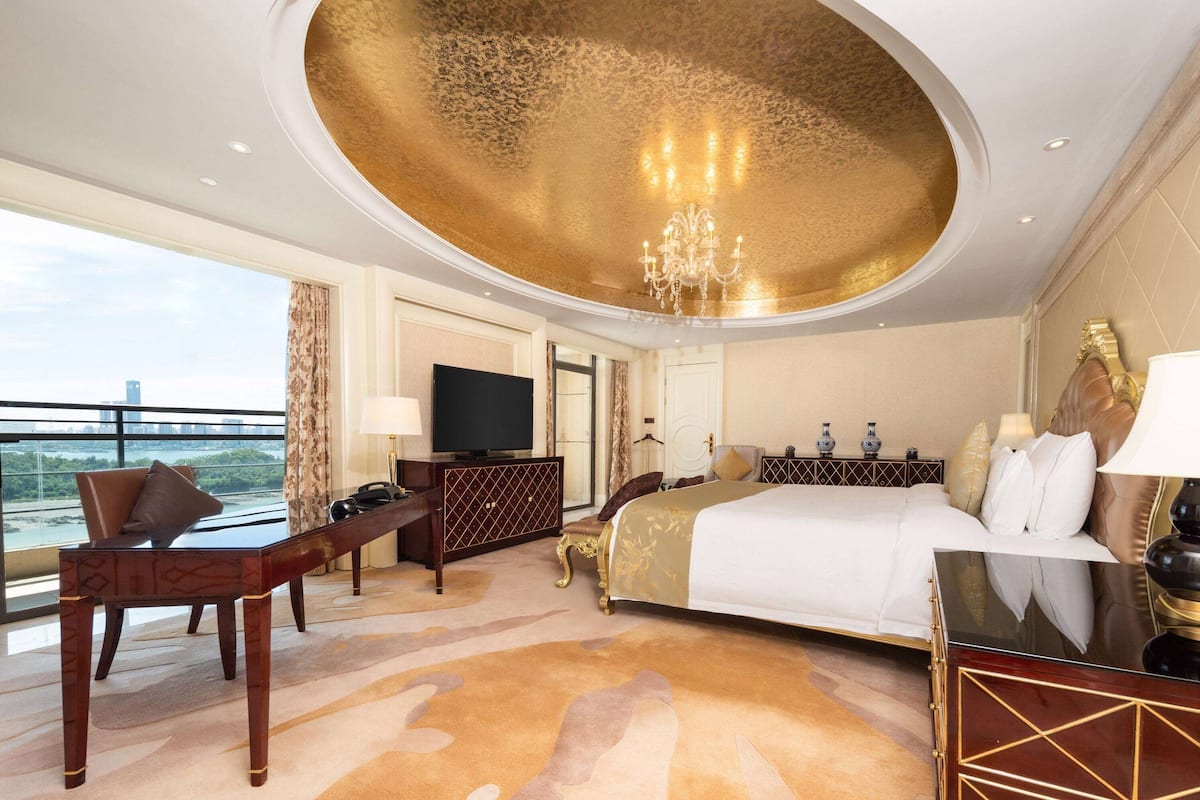 A spacious hotel room with a large bed, a desk, a television, and a view of the city.