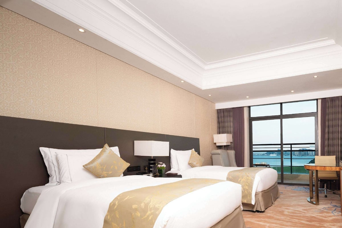 A hotel room with two beds, a desk, and a view of the water.