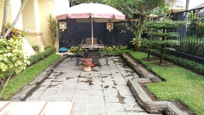 A patio area with a table and chairs, a potted plant, and a decorative umbrella. - Roemah Canting (Yogyakarta)