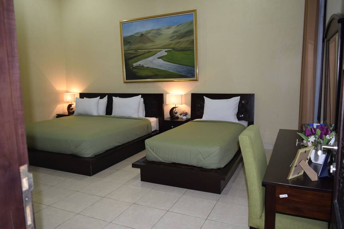A hotel room with two beds, a desk, and a painting of a landscape on the wall.