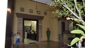 A lobby with a reception desk, a large green vase, and a child standing near the entrance. - Roemah Canting (Yogyakarta)