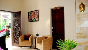 A room with two armchairs, a small table with a plant, a painting on the wall, and a door with a sign. - Roemah Canting (Yogyakarta)
