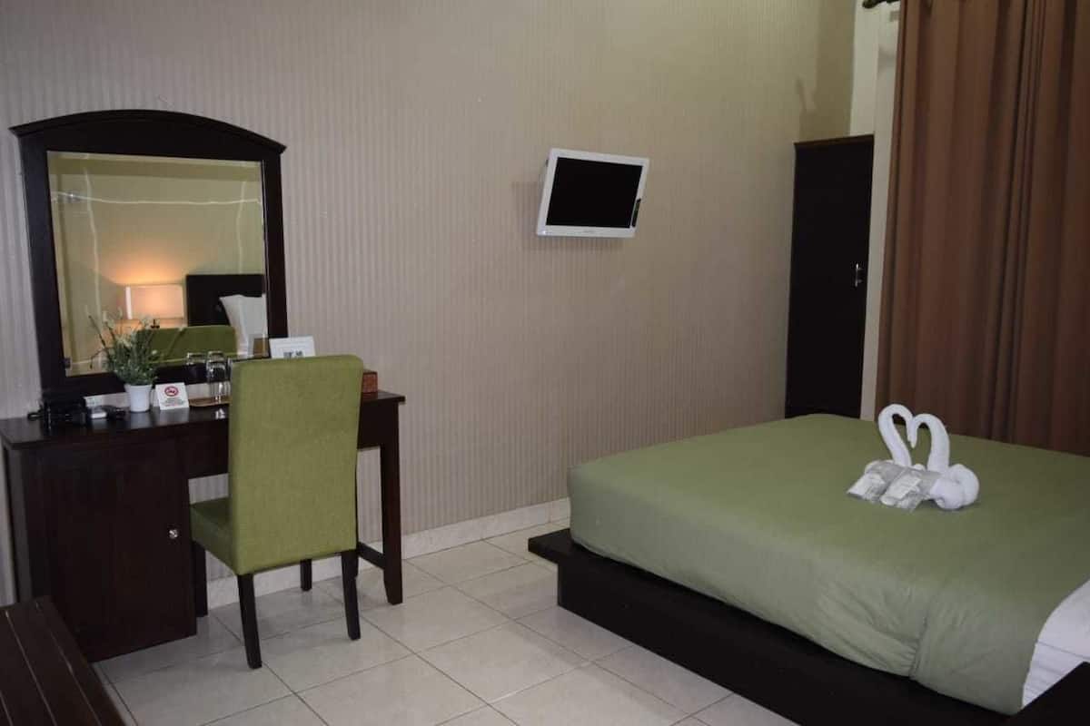 A hotel room with a bed, a desk with a chair, a mirror, a small TV, and a window with curtains.