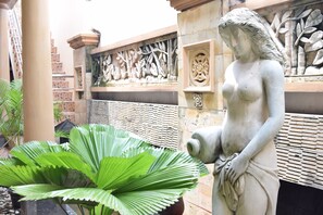 A statue in a courtyard with a large plant in the foreground. - Roemah Canting (Yogyakarta)