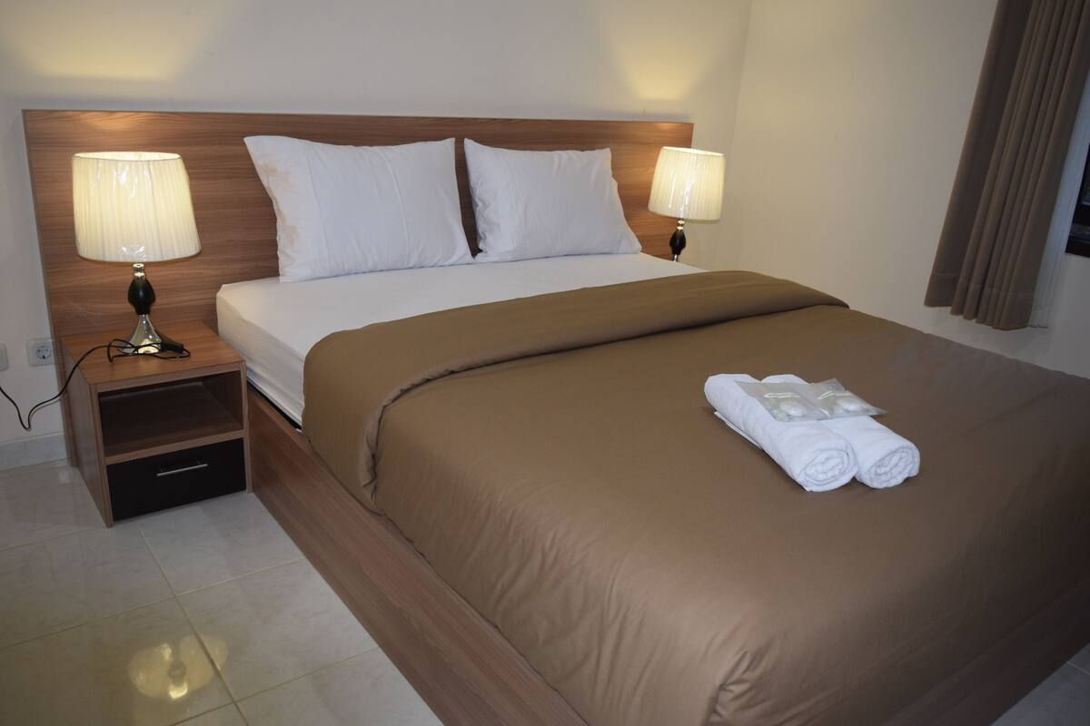 A neatly made bed with a brown bedspread and two white pillows, flanked by two bedside lamps on wooden nightstands.