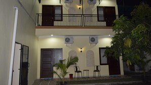 A two-story building with a balcony, air conditioning units, and a small garden area with chairs and a palm tree. - Roemah Canting (Yogyakarta)