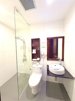 Ein Badezimmer mit einer gläsernen Dusche, einer weißen Toilette, einem Waschbecken mit blauem Blumendruck und einem Holzschrank darüber.