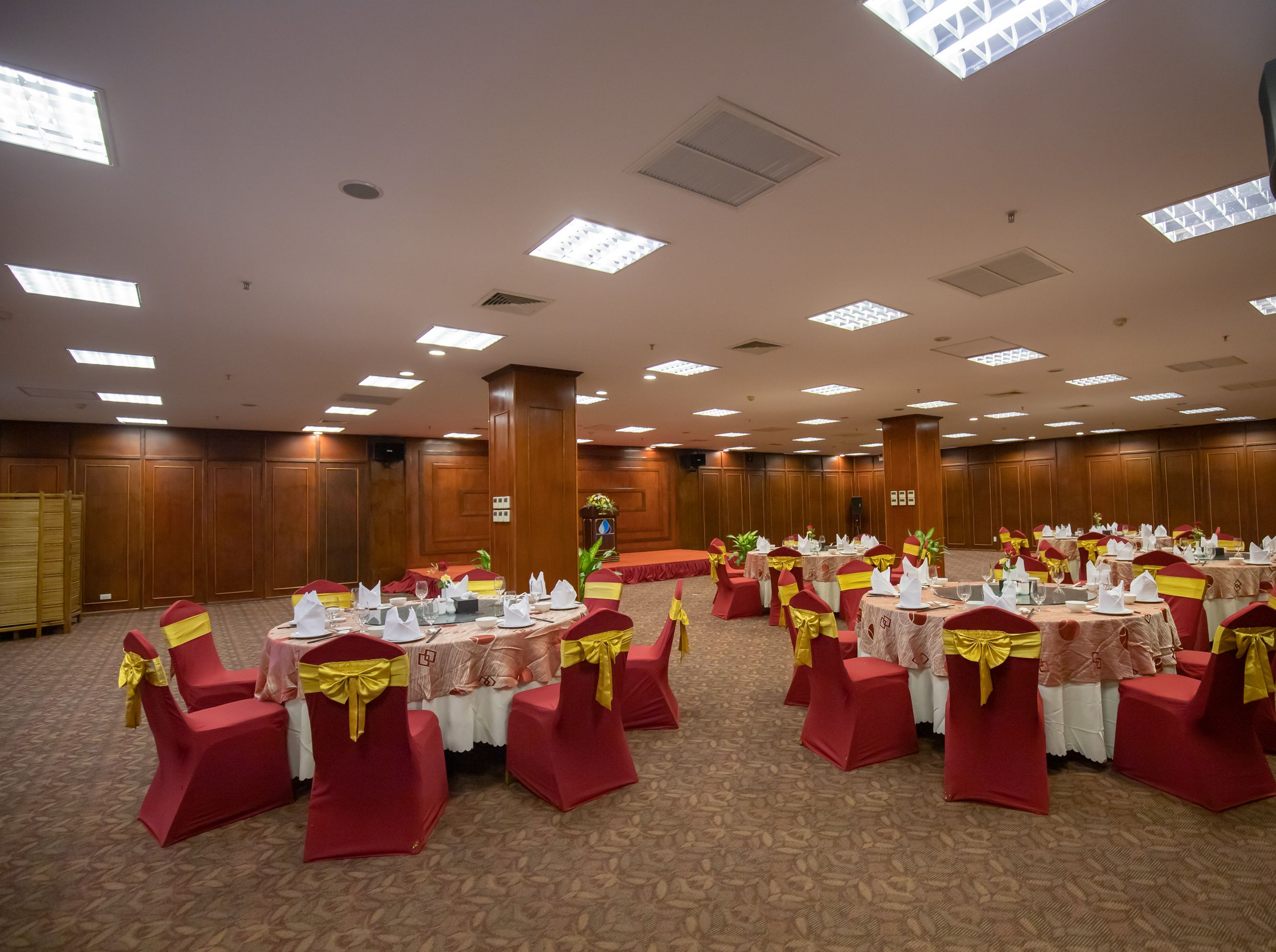 Un salón de banquetes con mesas redondas, sillas rojas y cintas amarillas.