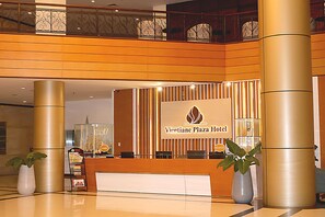 Ein Empfangsschalter mit einem Schild für das Vientiane Plaza Hotel, zwei große Säulen und ein dekoratives Modellschiff.