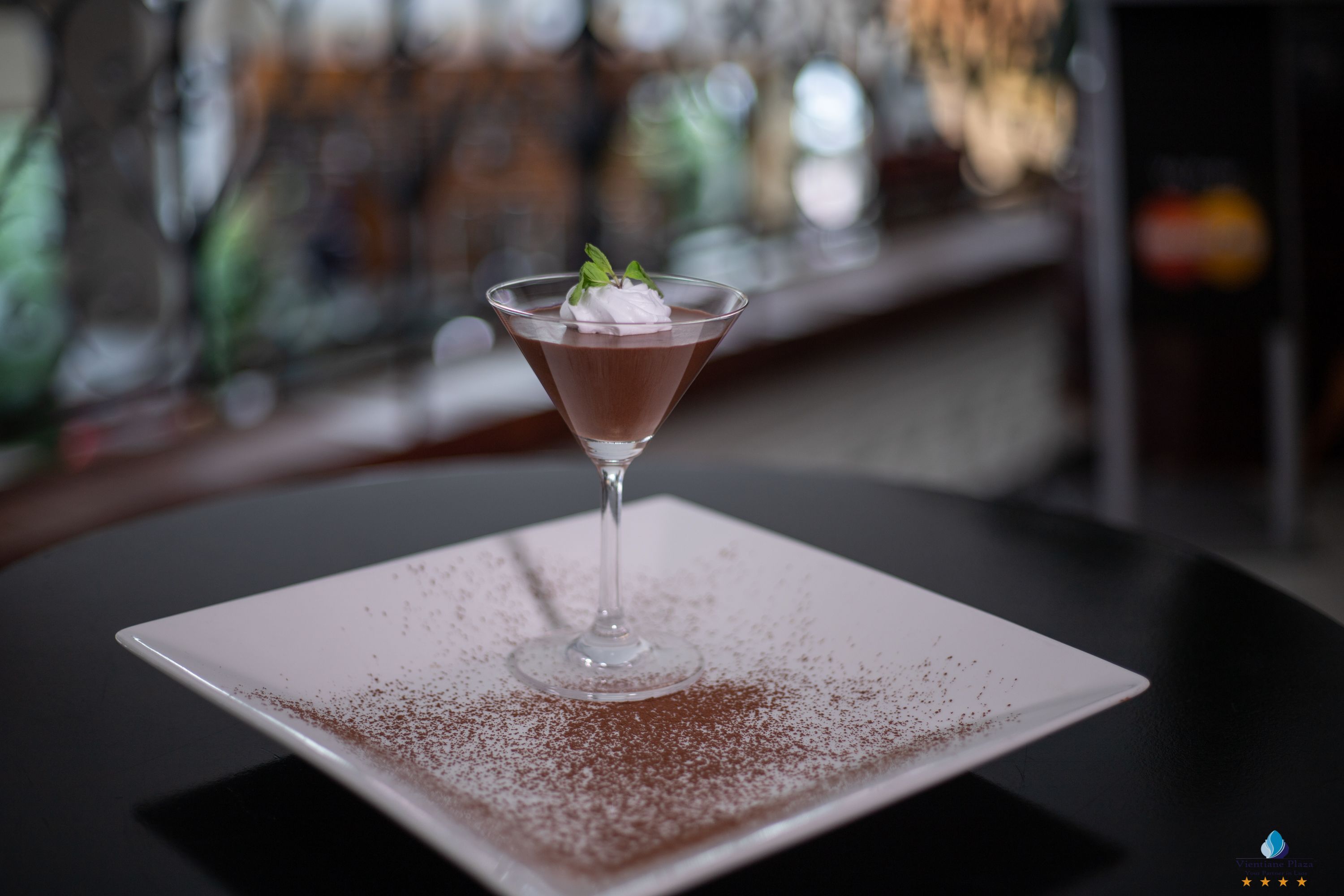 A dessert in a martini glass on a square plate with a dusting of cocoa powder.