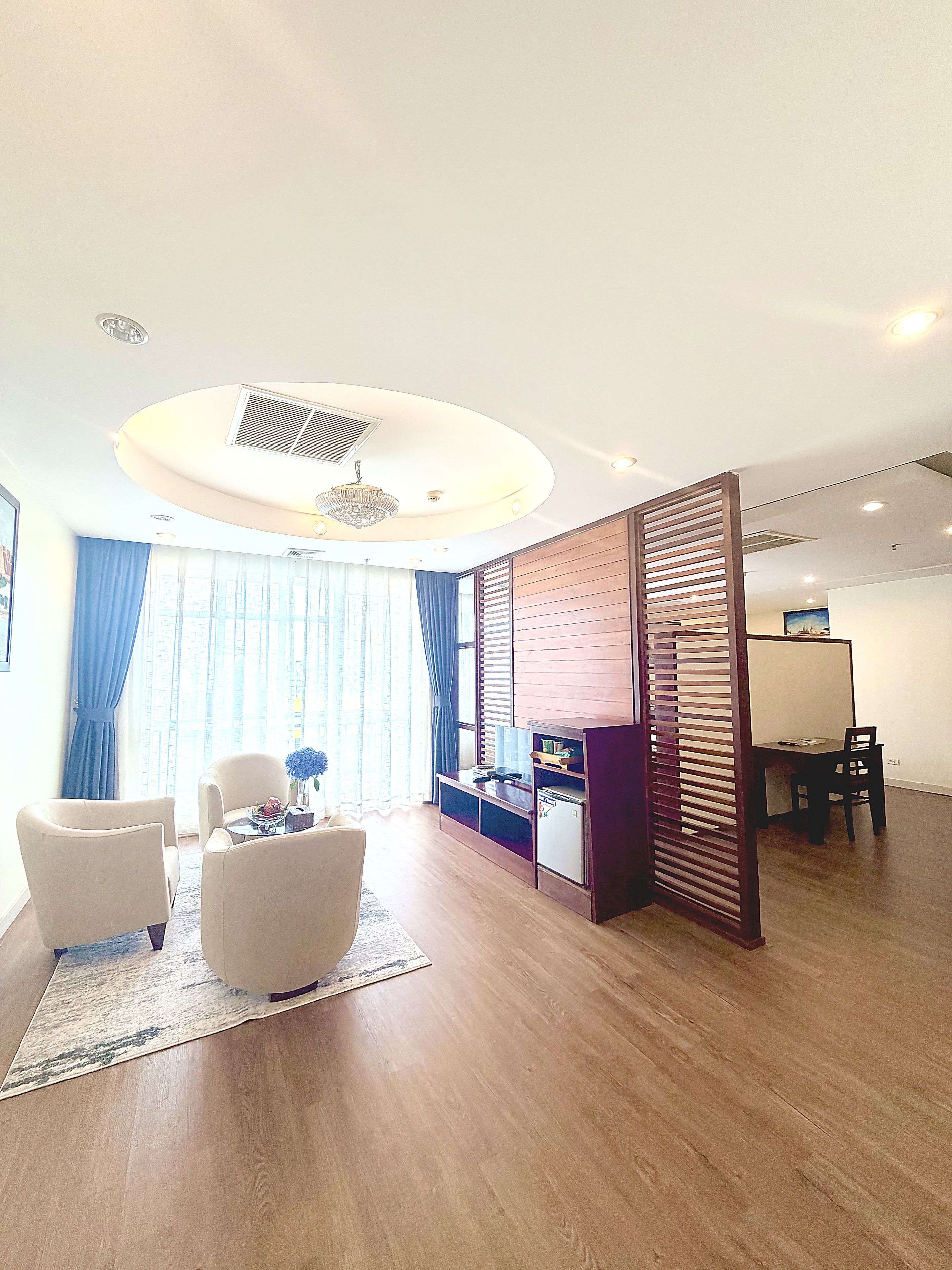 A modern living room with a round ceiling light, a wooden partition, and a dining area with a table and chairs.