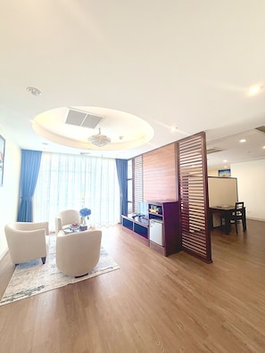 Una sala de estar moderna con una lámpara de techo redonda, un separador de madera y un comedor con mesa y sillas.
