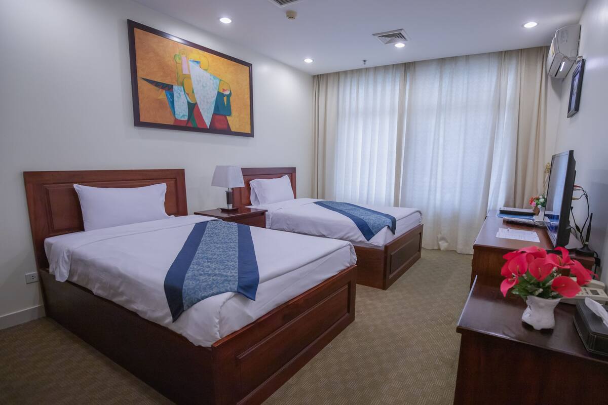 Een hotelkamer met twee bedden, een bureau met een computer, een lamp en een schilderij aan de muur.