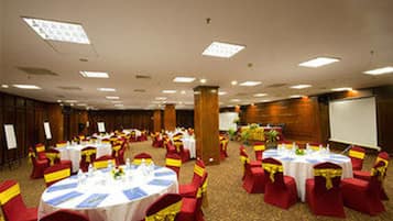 A banquet hall with round tables, red chairs, and yellow sashes.