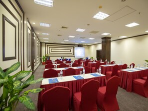 A conference room with rows of red chairs, tables with water bottles, and a projector screen. - Vientiane Plaza Hotel (Vientiane)
