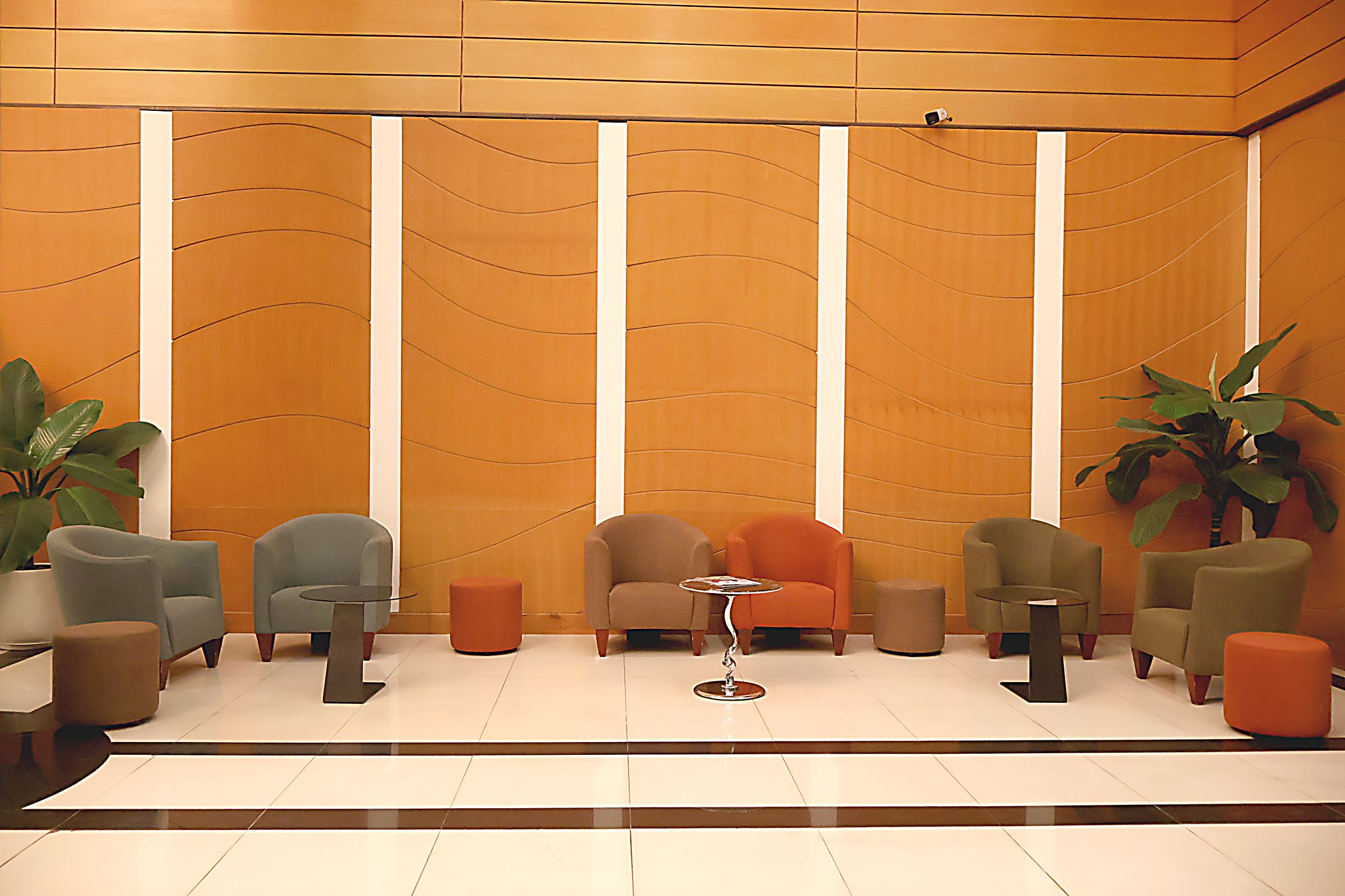 A lobby with a modern design, featuring a seating area with multiple chairs and tables, a large potted plant, and a decorative wall with vertical lines.