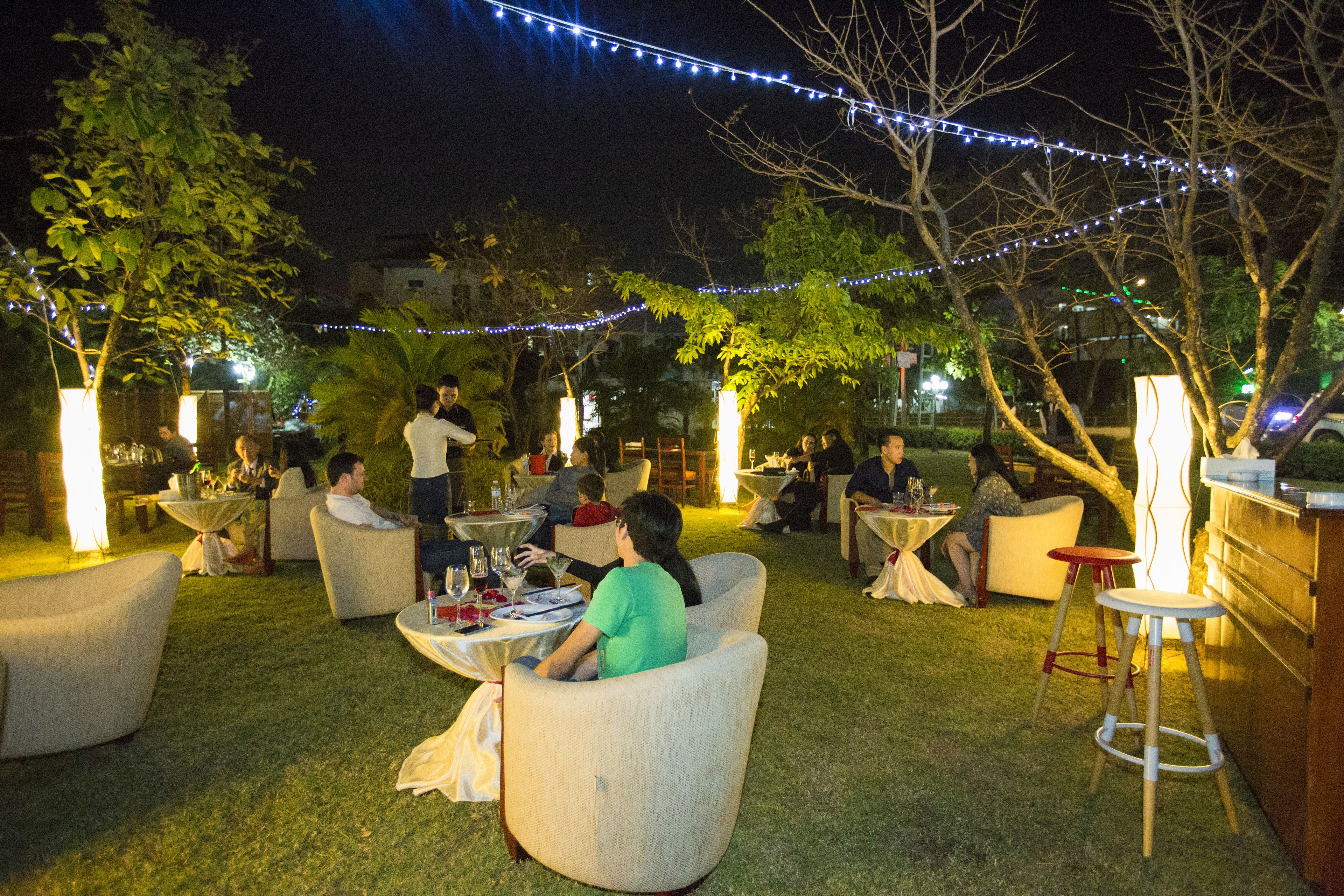 An outdoor seating area with tables and chairs, surrounded by trees and string lights.