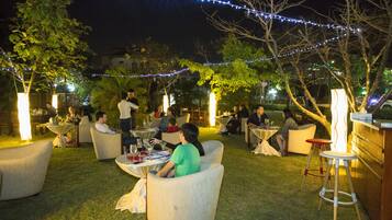An outdoor seating area with tables and chairs, surrounded by trees and string lights.