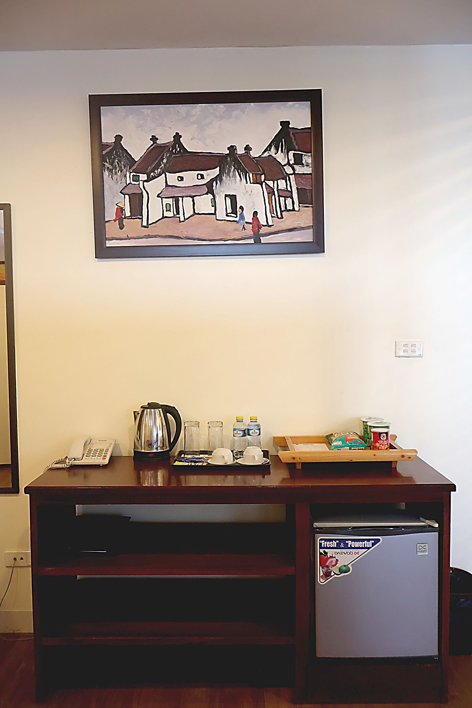Een kamer met een houten bureau, een koelkast, een schilderij aan de muur en een telefoon.