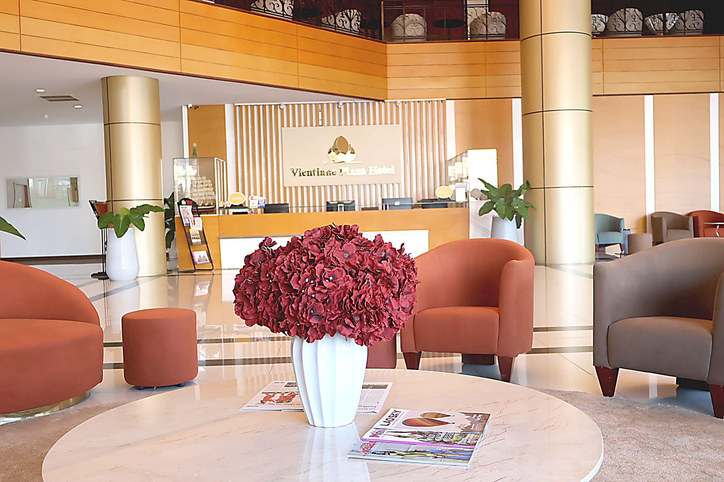 A hotel reception area with a reception desk, a large vase of flowers, and seating arrangements.