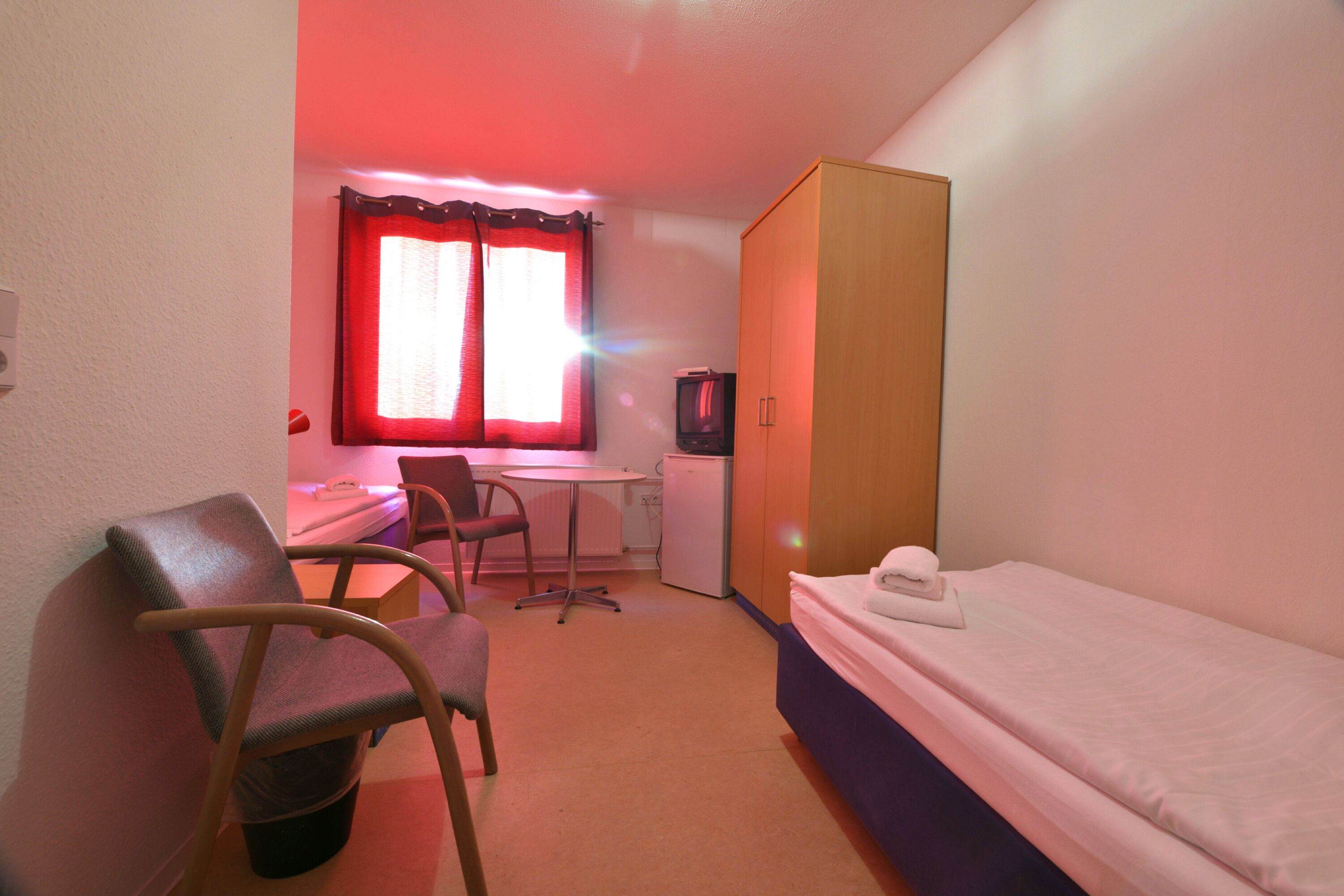 A small room with a single bed, a desk, a chair, and a television.